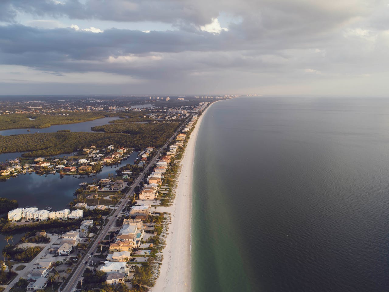Stunning aerial view of coastal homes lining a serene beach with the ocean and clouds in the distance.