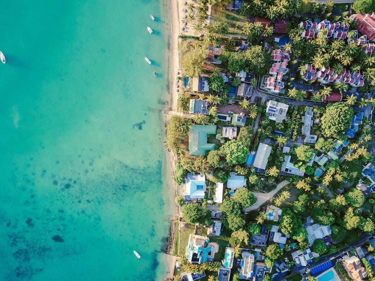 A stunning aerial view of a vibrant tropical coastal village with turquoise waters and lush greenery.